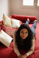 Indian woman laying down on red sofa and smiling. - Asia Images Group