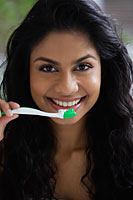 Head shot of Indian woman brushing her teeth and smiling. - Asia Images Group