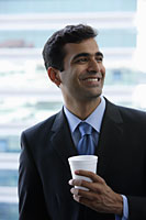 Head shot of Indian businessman holding cup and smiling. - Asia Images Group
