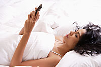 Indian woman laying down in bed looking at phone. - Asia Images Group