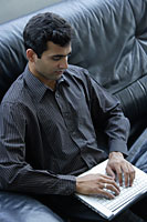 Indian businessman sitting on black sofa with laptop. - Asia Images Group