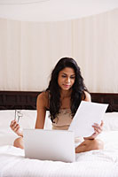Indian woman sitting on bed working on laptop - Asia Images Group