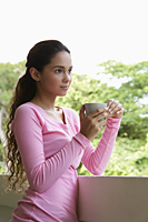 Young woman holding cup leaning on balcony - Asia Images Group