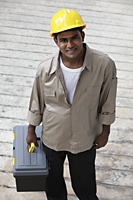man wearing construction hat and holding tool box and smiling - Asia Images Group