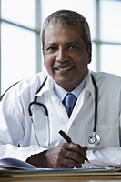 Indian doctor sitting at desk and smiling - Asia Images Group
