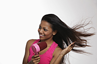 woman blow drying her long hair and smiling - Asia Images Group