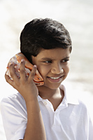 young boy listening to sea shell and smiling - Asia Images Group