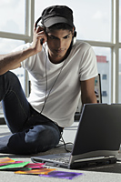 young man listening to music while looking at laptop - Asia Images Group