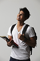 young man looking up, wearing back pack and holding books. - Asia Images Group