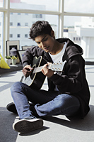 young man sitting on floor playing guitar - Asia Images Group