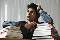 young man with a stack of books thinking - Asia Images Group