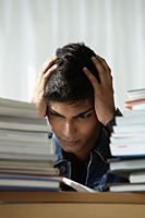 young man holding head and reading book - Asia Images Group
