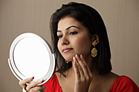 head shot of woman looking at her face in the mirror - Asia Images Group