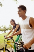 Two young men on bicycles, side by side, looking away - Asia Images Group