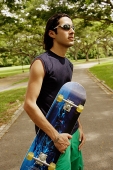 Man wearing sunglasses, holding skateboard - Asia Images Group