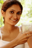 Woman smiling at camera, holding glass of water - Asia Images Group