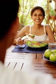 Woman at table with plate of salad, looking at man across from her - Asia Images Group