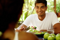Man looking at person opposite him, salad in front of him - Asia Images Group