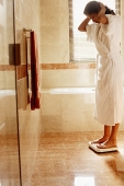 Woman in bathroom, wearing bathrobe, standing on weight scale - Asia Images Group