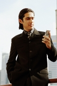 Businessman looking at mobile phone, hands in pocket - Asia Images Group