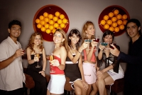Young adults in night club, holding drinks out towards camera - Asia Images Group