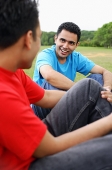 Two men sitting side by side in park, talking - Asia Images Group