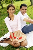 Couple in park, sitting on grass, looking at camera - Asia Images Group