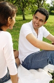 Couple sitting on picnic blanket, looking at each other - Asia Images Group