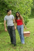 Couple walking in park, arm in arm, woman carrying picnic basket - Asia Images Group