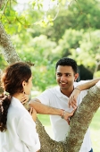 Couple looking at each other, standing on either side of tree - Asia Images Group