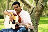 Young man sitting under tree, holding guitar, portrait - Asia Images Group