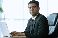 Businessman in office, sitting at desk, looking at camera - Asia Images Group
