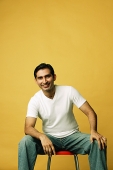 Man sitting on stool, smiling at camera, hand on knee - Asia Images Group