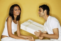 Couple sitting face to face, woman looking at camera, man holding gift - Asia Images Group