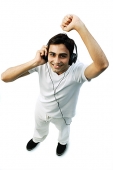 Young man listening to headphones, arm raised, smiling at camera - Asia Images Group