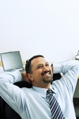 Businessman in office, hands behind head, smiling - Asia Images Group