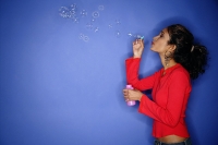 Woman blowing bubbles with bubble wand, side view - Asia Images Group
