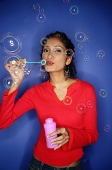 Woman blowing bubbles from bubble wand, looking at camera - Asia Images Group