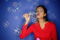 Woman blowing bubbles from bubble wand, bubbles all around her - Asia Images Group