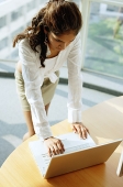 Woman standing over desk, using laptop - Asia Images Group