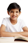 Boy leaning on book, smiling at camera - Asia Images Group