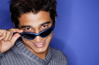 Man against blue background, adjusting sunglasses, smiling at camera - Asia Images Group