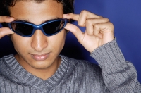 Man against blue background, adjusting sunglasses - Asia Images Group