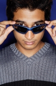 Man against blue background, adjusting sunglasses, looking at camera - Asia Images Group
