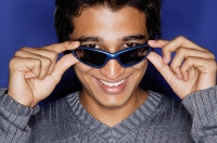 Man against blue background, adjusting sunglasses, smiling at camera - Asia Images Group