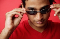 Man against red background, adjusting sunglasses, looking at camera - Asia Images Group