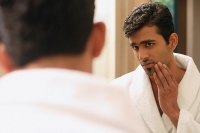 Man in bathrobe looking at himself in mirror, hand on chin - Asia Images Group