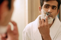 Man shaving his face, looking in mirror - Asia Images Group