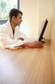 Man in bathrobe, looking at computer - Asia Images Group