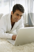 Man in bathrobe, using laptop, smiling - Asia Images Group